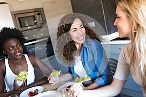 Group of friends laughing while eating healthy food at home.