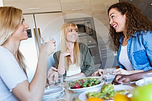 Group of friends laughing while eating healthy food at home.