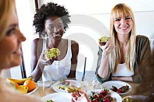 Group of friends laughing while eating healthy food at home.