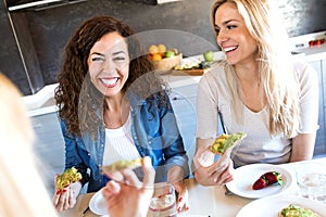 Group of friends laughing while eating healthy food at home.