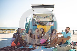 Group of friends looking at camera while sitting near camper van at beach