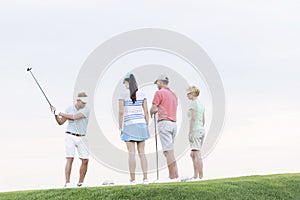 Group of friends looking at man playing golf against clear sky