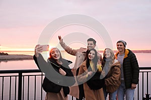 Group of friends making selfie near river at sunset