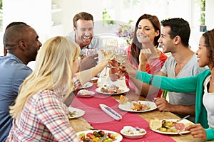 Group Of Friends Making Toast Around Table At Dinner Party