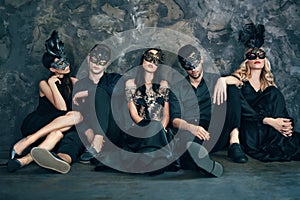 Group of friends in masquerade carnival mask sitting on floor relax after party