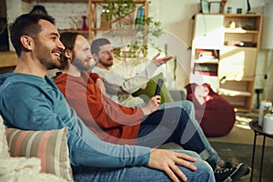 group of friends, men talking and having fun while watching TV sitting on sofa in living room at home. Concept of