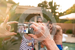 Group Of Friends Outdoors Relaxing By Swimming Pool Posing For Photo On Mobile Phone