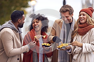 Group Of Friends Outdoors Wearing Coats And Scarves Eating Takeaway Fries In Autumn London