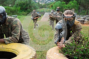 Group of friends paintball players of opposite teams in shootout in forest