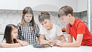 Group of friends play toy fishing on kitchen table. Smart boy hold fishing rod and pick up playthings from plate.