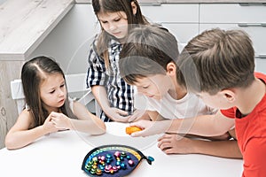 Group of friends play toy fishing on table. Child hold fishing rod and pick up colorful metal playthings from plate.