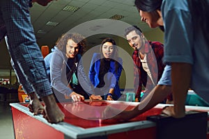 A group of friends playing air hockey in an amusement park.