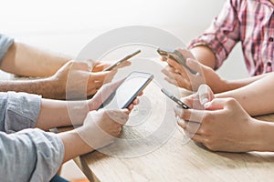 Group of friends playing app games in mobile phone and online together. Hands are holding smartphone circle on the table