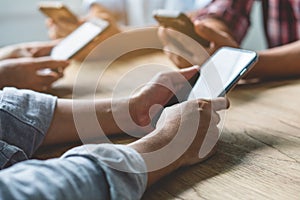 Group of friends playing app games in mobile phone and online together. Hands are holding smartphone circle on the table