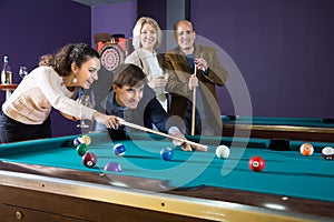 Group of friends playing billiards and smiling in billiard room