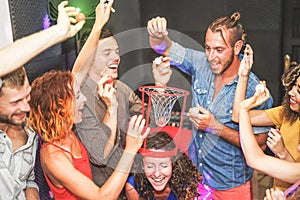 Group of friends playing funny basketball games inside a pub cocktail bar - Young happy people having fun hangout in the weekend