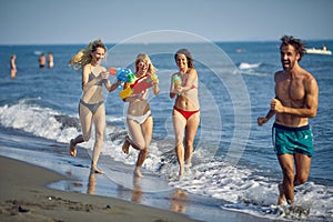 Group of friends playing with water guns at beach together. Young adults on summer vacation. Holiday, fun, travel, lifestyle