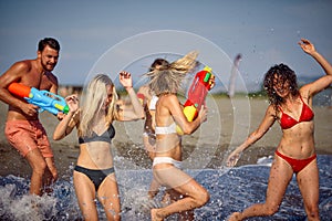 Group of friends playing with water pistols in water at beach. Young adults on summer vacation together having water gun battle.