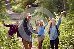 Group Of Friends Posing For Selfie In Countryside Taking Picture On Phone As They Hike Along Path
