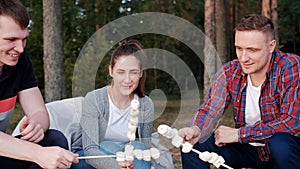 A group of friends relax in a forest camp. Men and women prepare a marshmallow on a bonfire. A party in nature.