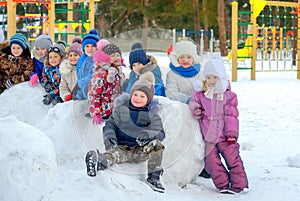 Group of friends are resting on large snowballs, on a winter playground