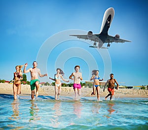 Group of friends run in the sea with aircraft in the sky. Concept of summertime