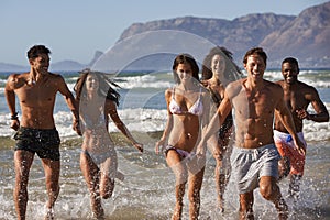 Group Of Friends Run Through Waves Together On Beach Vacation