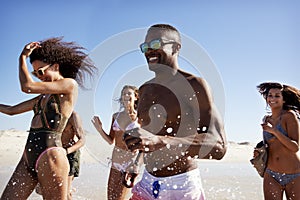 Group Of Friends Run Through Waves Together On Beach Vacation