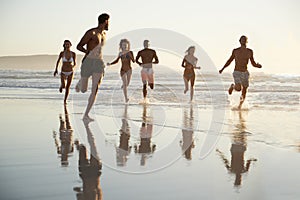 Group Of Friends Run Through Waves Together On Beach Vacation