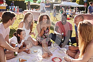 Group Of Friends Sitting On Rug At Summer Garden Fete With Drinks