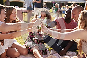 Group Of Friends Sitting On Rug At Summer Garden Fete And Making Toast