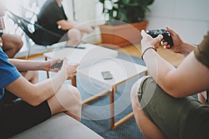 Group of friends sitting on a sofa in living room and playing video games. Family relaxing time at home concept.