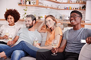 Group Of Friends Sitting On Sofa And Watching Movie At Home Whilst Drinking Wine