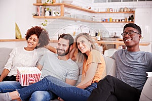 Group Of Friends Sitting On Sofa And Watching Movie At Home Whilst Eating Popcorn