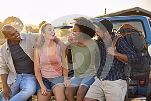 Group Of Friends Sitting On Tailgate Of Pick Up Truck On Road Trip To Cabin In Countryside