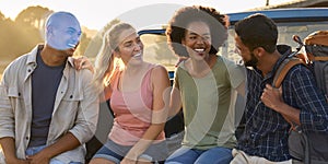 Group Of Friends Sitting On Tailgate Of Pick Up Truck On Road Trip To Cabin In Countryside