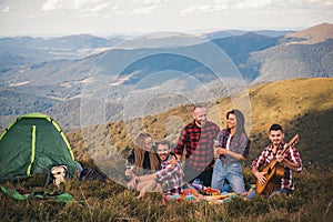 Group of friends sitting together on mountain top. Young people enjoying on their holiday outdoors. Happy friends are