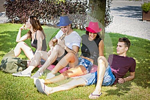 Group of friends sitting under tree, playing guitar