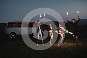 A group of friends with sparklers standing outdoors at dusk.