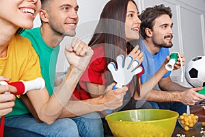 Group of friends sport fans watching match in colorful shirts holding noisemakers close-up