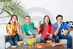 Group of friends sport fans watching match in colorful shirts holding noisemakers