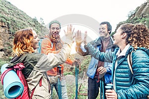 Group of friends stacking hands while doing trekking excursion on mountain - Young tourists walking and exploring the wild nature