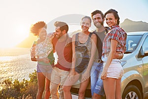 Group Of Friends Standing By Car On Coastal Road At Sunset