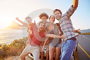 Group Of Friends Standing By Car On Coastal Road At Sunset