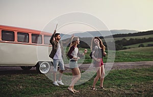 A group of friends standing outdoors on a roadtrip through countryside, dancing.