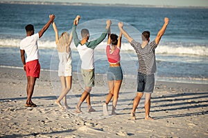 Group of friends standing with raised hands on the beach