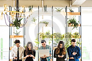 Group of friends standing on table and everyone use his divices in modern office room. Together fun in device.