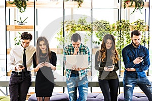 Group of friends standing on table and everyone use his divices in modern office room. Together fun in device.