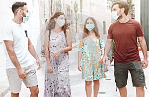 Group of friends stroll through city streets wearing surgical masks - people walk wearing protective equipment during the