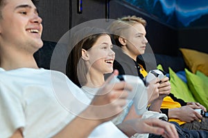 Group of friends of teenagers, boys and girls playing video games on a console in a game club